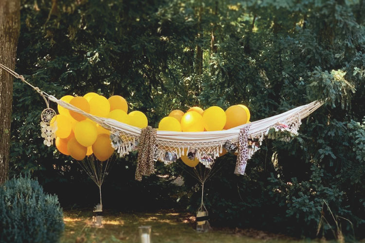 Weiße Hängematte gespannt zwischen Bäumen und gelbe Luftballons im Hintergrund